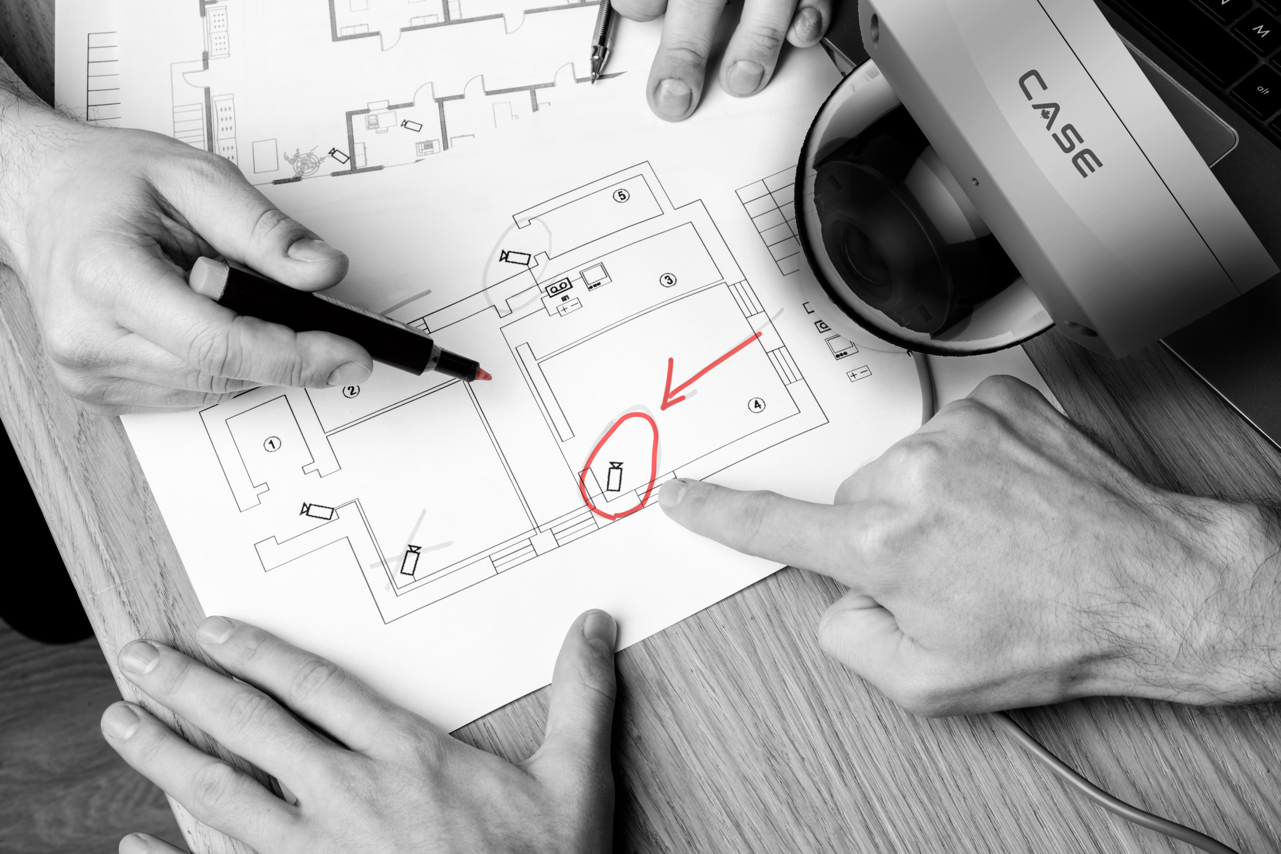 Two people discussing CCTV project. Video security equipment and blueprint on a table